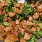 Bowl of orange chicken stir fry with broccoli, topped with sesame seeds and served over cauliflower rice.