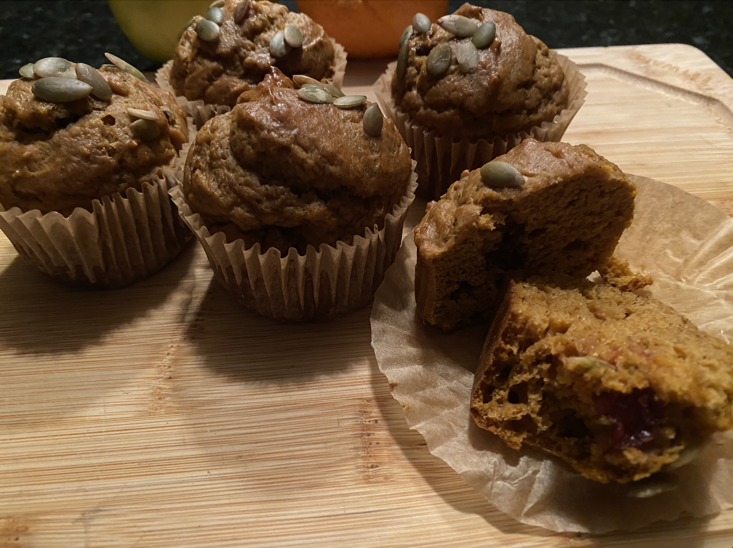 Freshly baked cranberry pumpkin muffins topped with pumpkin seeds on a cooling rack, surrounded by fall leaves and a small bowl of maple cream cheese.