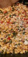 Close-up of colorful Mexican street corn in a skillet, garnished with cilantro, green onions, and crumbled cotija cheese.