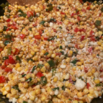 Close-up of colorful Mexican street corn in a skillet, garnished with cilantro, green onions, and crumbled cotija cheese.