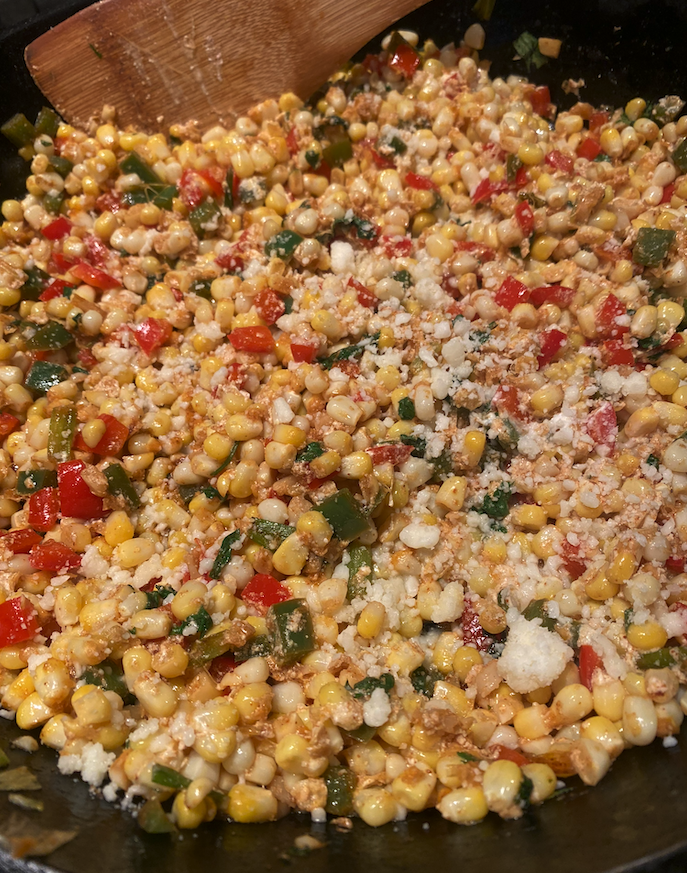 Close-up of colorful Mexican street corn in a skillet, garnished with cilantro, green onions, and crumbled cotija cheese.