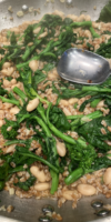 Bowl of broccoli rabe with white beans and farro, topped with Parmesan cheese and a drizzle of olive oil.