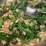 Bowl of broccoli rabe with white beans and farro, topped with Parmesan cheese and a drizzle of olive oil.