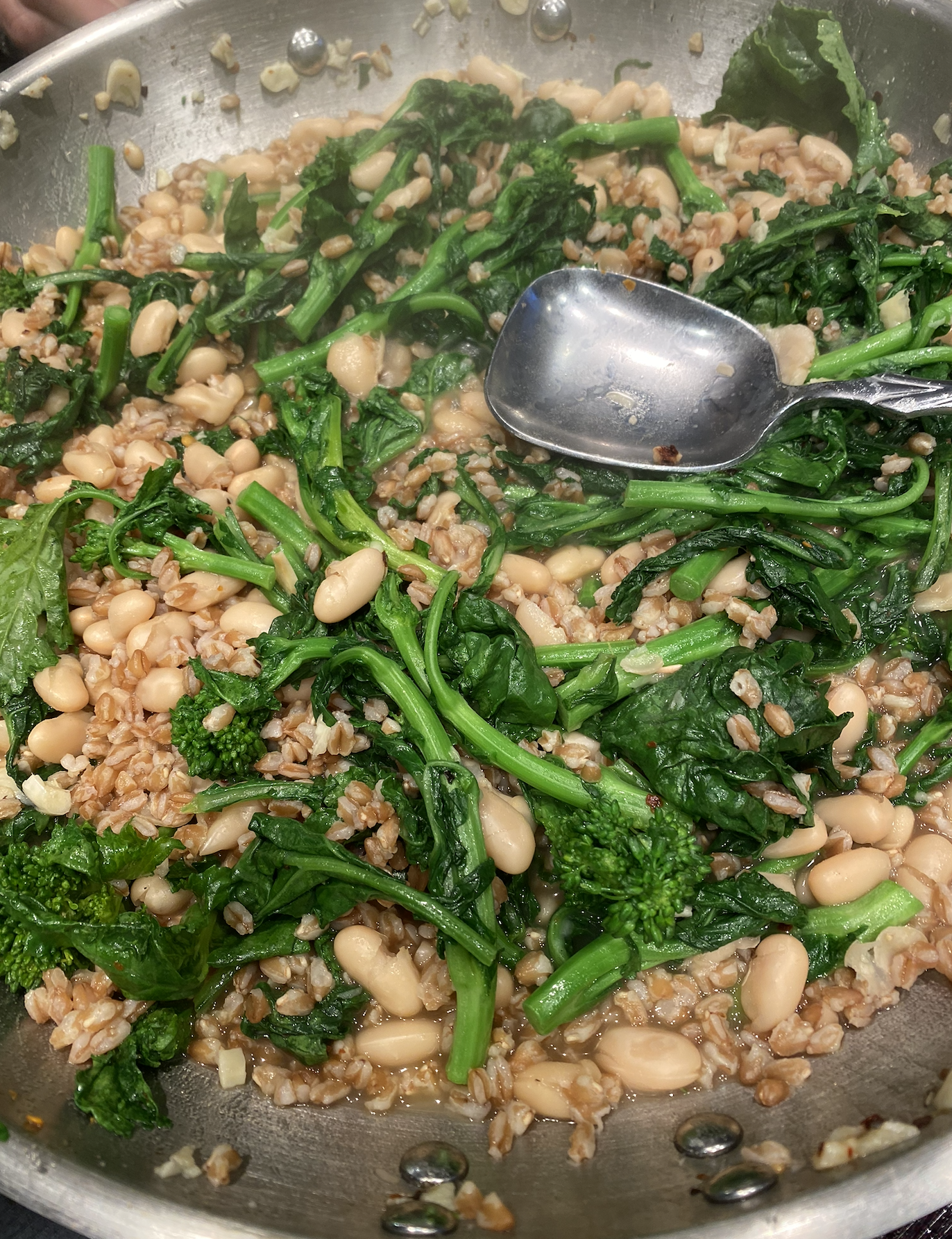 Bowl of broccoli rabe with white beans and farro, topped with Parmesan cheese and a drizzle of olive oil.