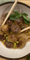 Thai coconut curry meatballs simmering in a creamy red curry sauce, garnished with basil and served over soba noodles.