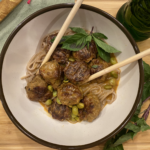 Thai coconut curry meatballs simmering in a creamy red curry sauce, garnished with basil and served over soba noodles.