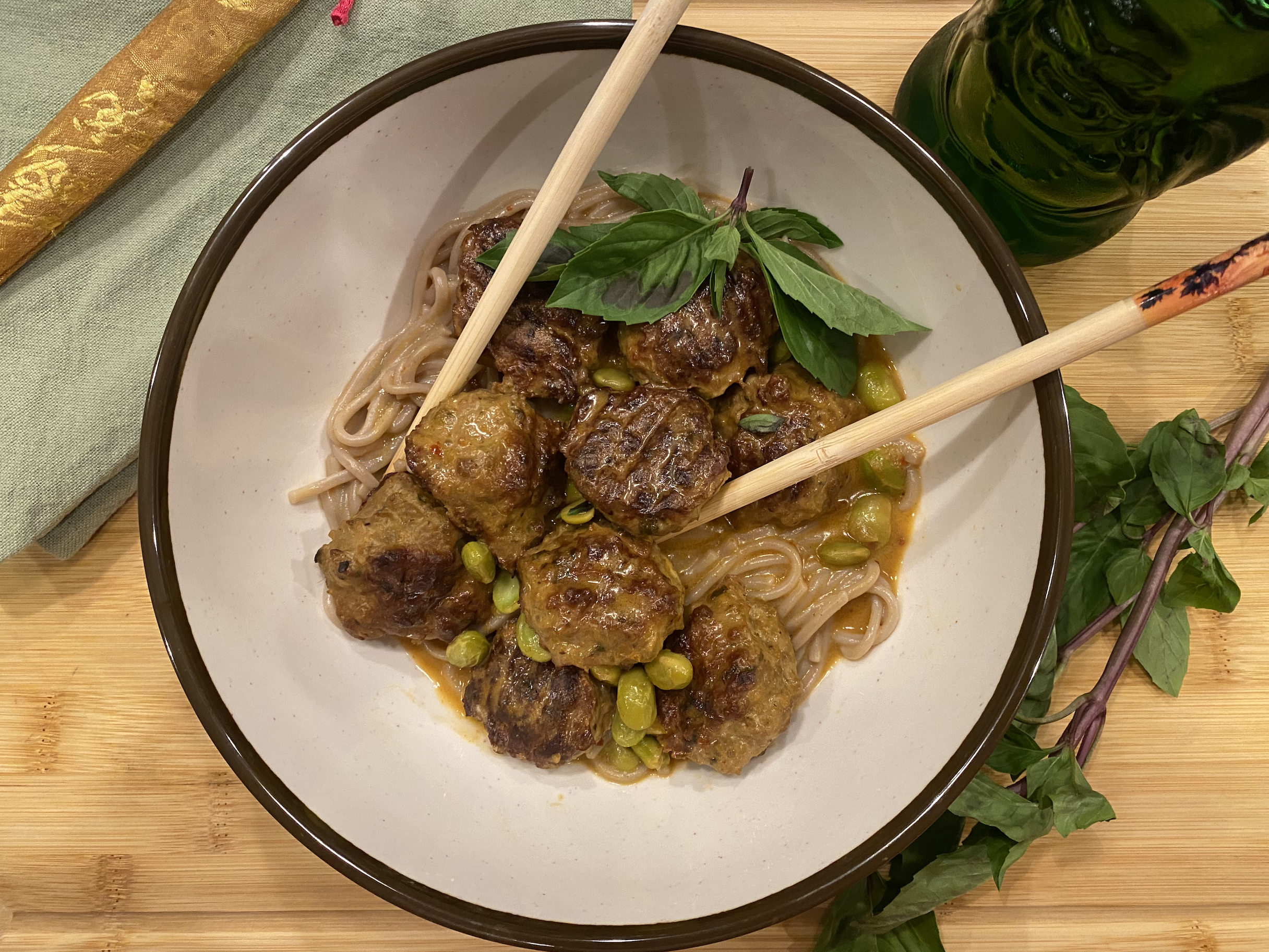Thai coconut curry meatballs simmering in a creamy red curry sauce, garnished with basil and served over soba noodles.