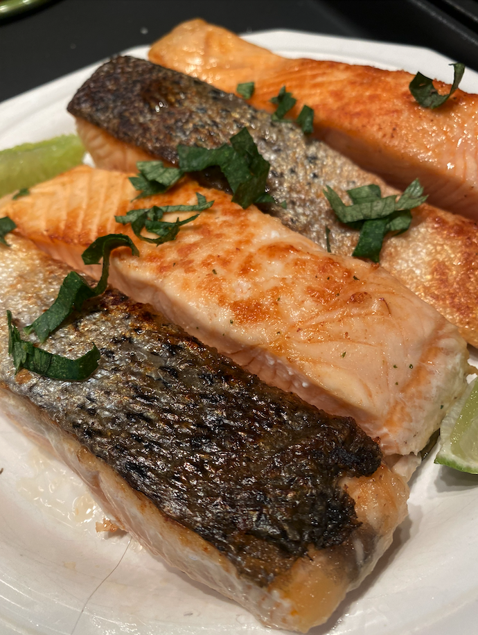 Crispy pan-seared fish filet topped with avocado sauce, diced tomato, and cilantro, served with a lemon wedge on a white plate.