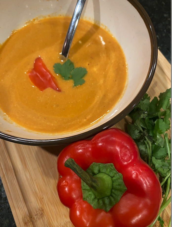 Creamy roasted red pepper soup with citrus and cashew cream in a white bowl.